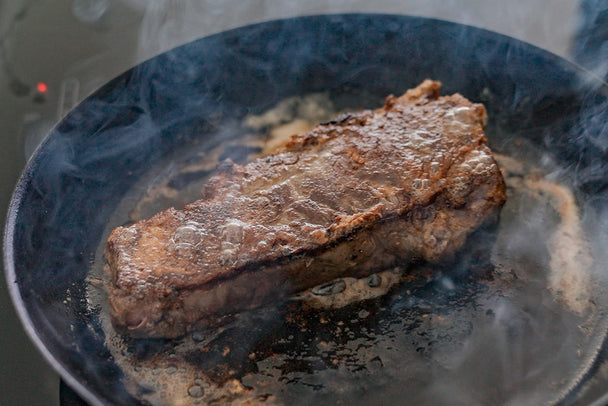A pan-seared steak sizzling in a cast iron pan.