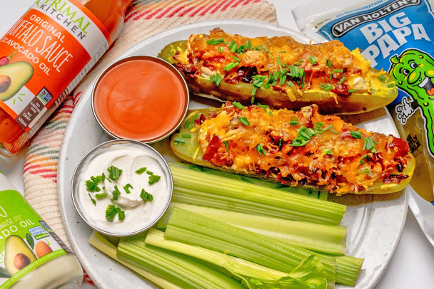 A plate of buffalo chicken stuffed pickles with Primal Kitchen Buffalo Sauce and a VanHolten dill pickle in the background.