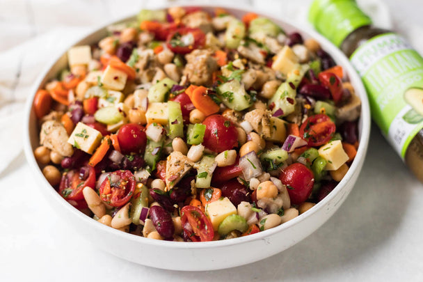 A colorful, delicious dense bean salad in a bowl next to a bottle of Primal Kitchen Italian Dressing