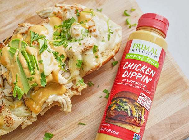 An open-faced chicken sandwich on a cutting board next to a bottle of Primal Kitchen Chicken Dippin sauce.