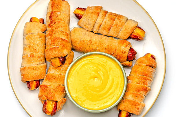 6 pretzel dogs on a white plate with a ramekin of Chicken Dippin' Sauce.
