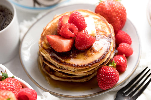 A takk stack of protein pancakes topped with berries, on a white plate