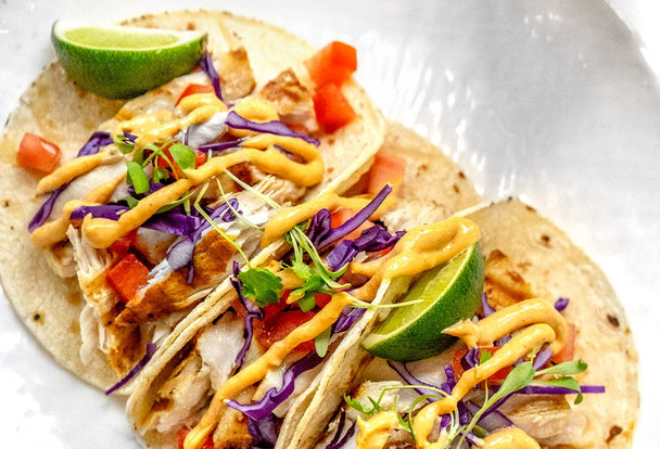 Three tilapia fish tacos on a white plate.