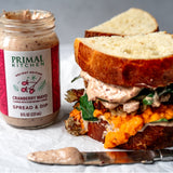 Leftover Thanksgiving dinner sandwich smothered in cranberry mayo next to a silver knife and an unopened jar of Primal Kitchen Cranberry Mayo.