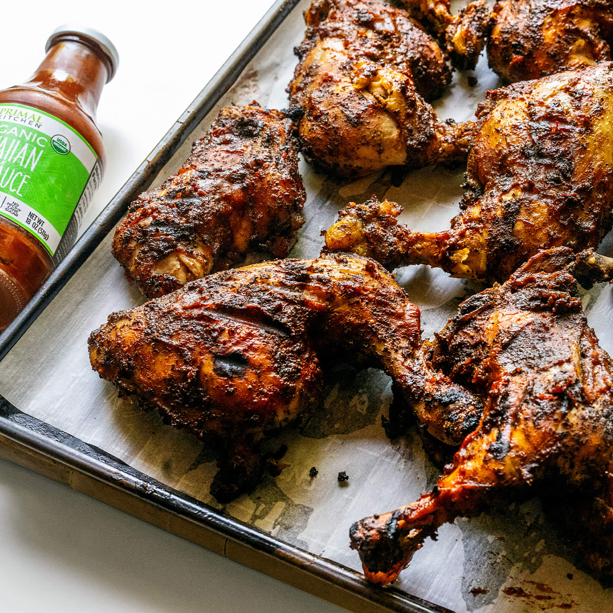 Hawaiian BBC Chicken Thighs on a sheet pan with Primal Kitchen Organic Hawaiian BBQ Sauce bottle in the background