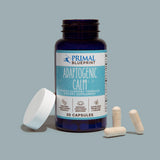 An uncapped blue bottle of Primal Blueprint Adaptogenic Calm next to a white lid and white supplements against a light blue background.