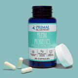 A blue bottle of Primal Blueprint Primal Probiotics uncapped with white supplements and a lid on the side against a light blue background.