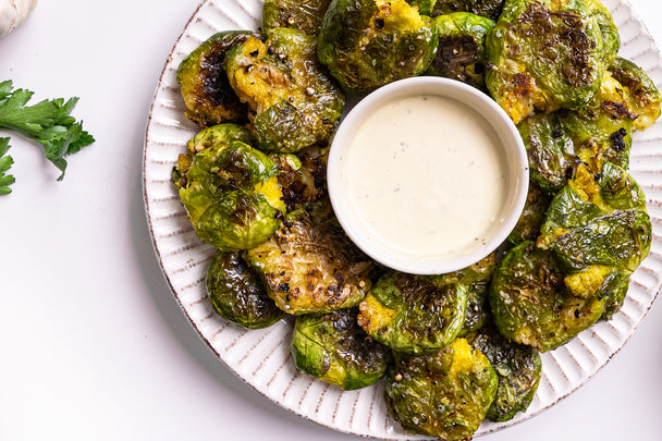 A white plate holds smashed Brussels sprouts around a ramekin of ranch dip.