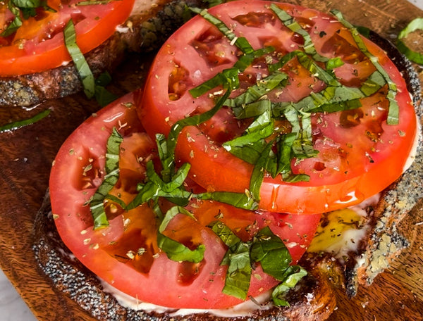 Closeup on fresh tomato toast made with Primal Kitchen Mayo and Extra Virgin Olive Oil, on a wooden board.