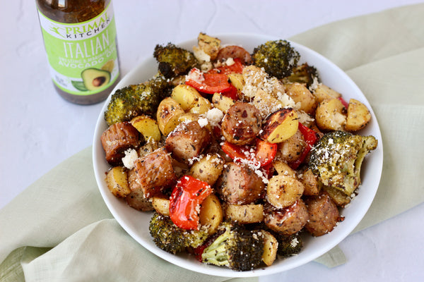 A bowl of chicken sausage, potatoes and veggies cooked on a sheet pan, with Primal Kitchen Italian Dressing in the background. 