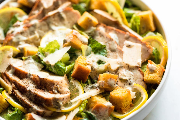 Closeup of a Chicken Caesar Salad made with Primal Kitchen Dressing, in a white bowl.