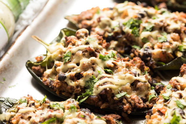 Stuffed poblano peppers topped with melted cheese, on a metal baking tray.