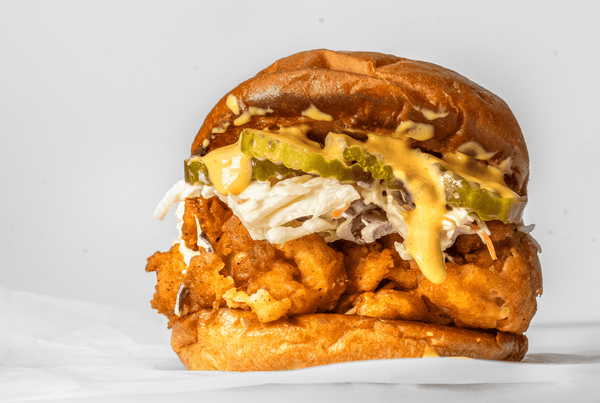 A mouthwatering crispy chicken sandwich with pickles and coleslaw, drizzled with Primal Kitchen Chicken Dippin’ Sauce. 