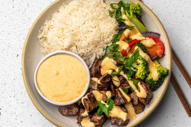 A beef kabob bowl with steak pieces, veggies, and rice drizzled with Primal Kitchen Yum Yum Sauce, with a container of extra sauce for dipping. 
