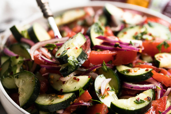 Closup on a bowl of cucumber tomato onion salad made with balsamic vinaigrette.