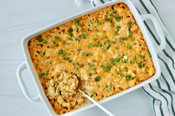 Buffalo chicken mac and cheese in a white baking dish, on a marble background with a striped towel.