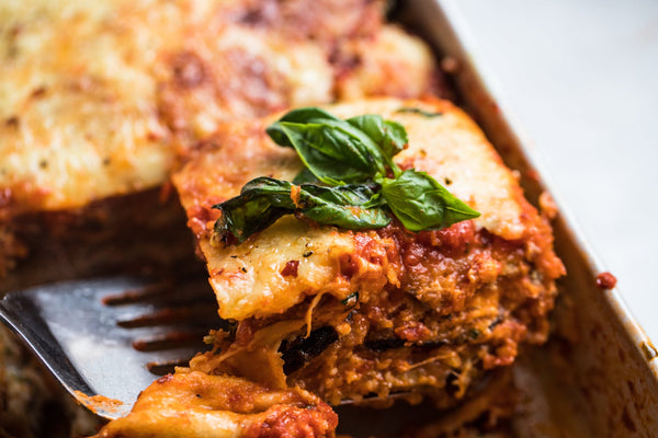 A spatula digging into a tray of eggplant parmesan made with Primal Kitchen Tomato Basil Pasta Sauce. 