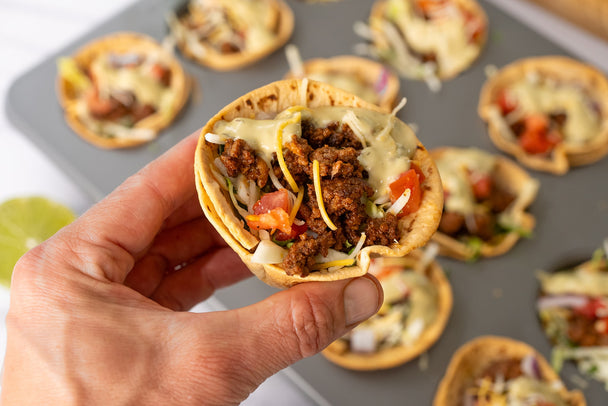 A hand holding a taco salad cup over a muffin tin of taco salad cups.