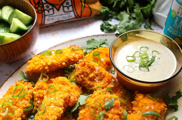 Crunch chicken tenders on a plate with ramekin of Primal Kitchen Ranch Dressing. LesserEvil Cheezmos in background.