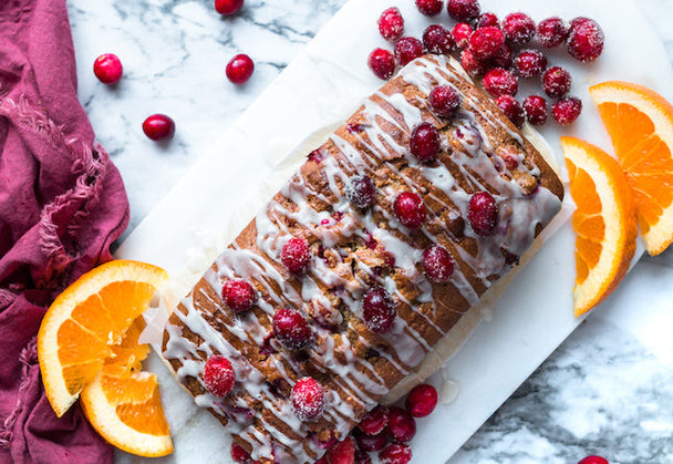 Glazed Cranberry Orange Olive Oil Cake on a white serving platter with orange slices and fresh cranberries.