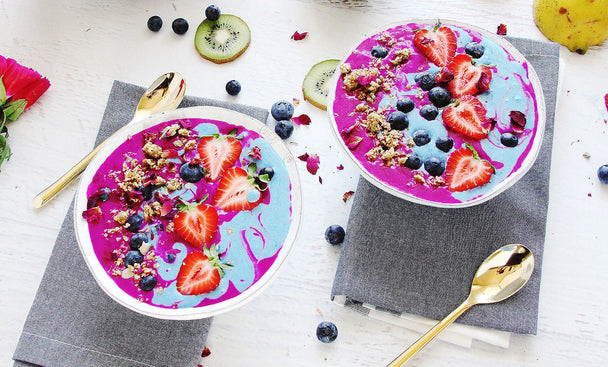 Two colorful pink and blue smoothie bowls topped with fresh berries and granola.