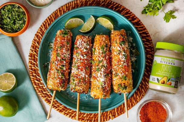 A white dish of grilled corn on the cob topped with cheese crumbles and mayo. 