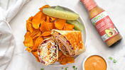 Rachel sandwich wrap served with chips and pickle spears alongside a bottle of Primal Kitchen Thousand Island Dressing.