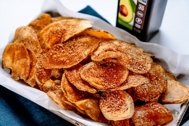 A basket of homemade potato chips with BBQ seasoning, with a bottle of Primal Kitchen Avocado Oil in the background.