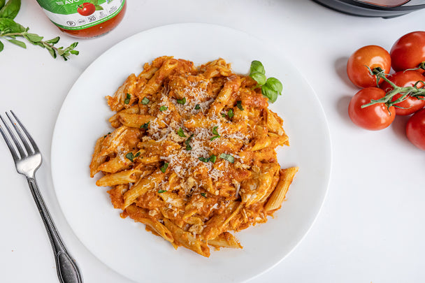 A white plate holds a serving of chicken parmesan pasta with a fork, sauce, and ingredients nearby.