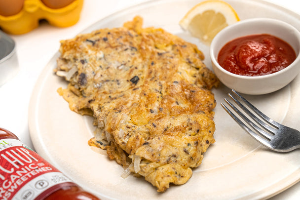 Primal Kitchen Ketchup is next to a plate with a omelet, ketchup and a lemon wedge on it and a fork resting nearby.