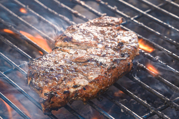 A steak covered in Primal Real Whipped Tangy Dressing & Spread cooking on a grill. 