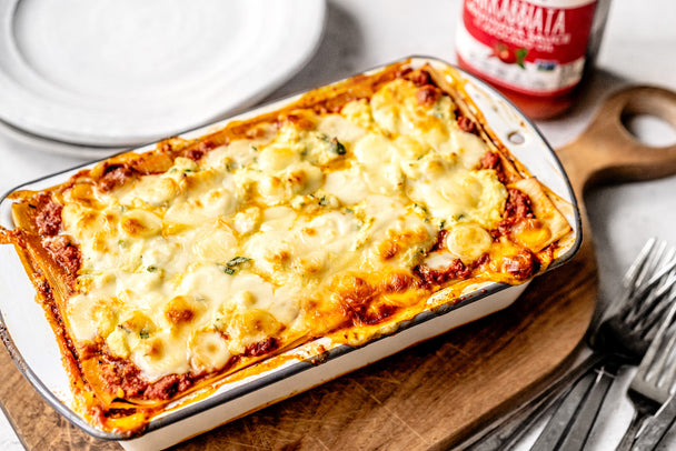 Keto spicy lasagna in a white baking dish next to silver forks and Primal Kitchen Arrabbiata Sauce