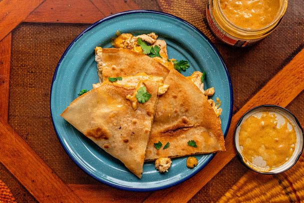 Queso dip is next to a blue plate of chicken quesadillas with cilantro and dip.