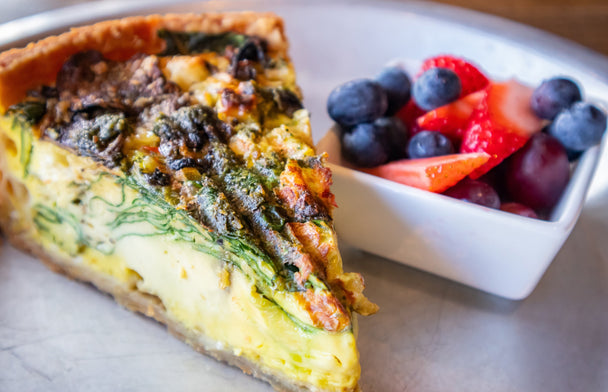 A spread of Eggs Benedict Quiche with eggs, creamer, hollandaise sauce, and other ingredients nearby, as well as egg crepes. 