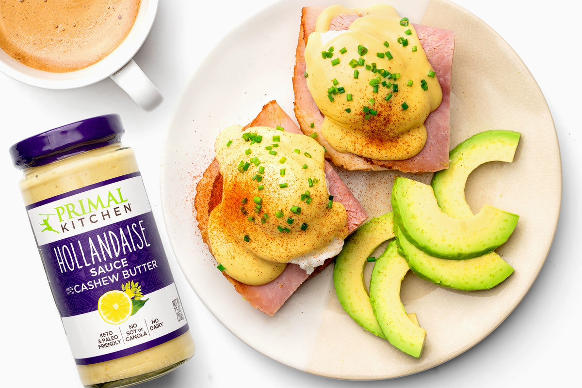 Hollandaise is next to a plate of eggs benedict with avocado slices.