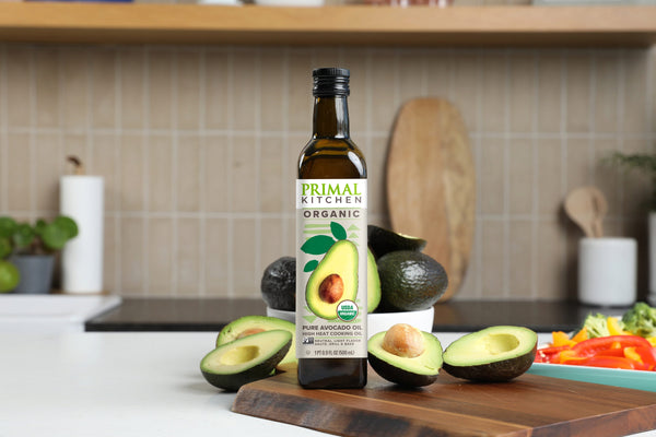 Primal Kitchen Organic Avocado Oil on a kitchen counter with avocado halves.