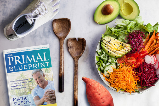 Primal Blueprint book alongside wooden spoons, salad bowl, and fitness shoes.