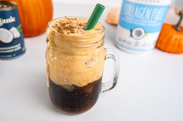 A mason jar holds a pumpkin cream cold brew next to a cannister of collagen fuel and pumpkins.