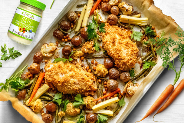 A sheet pan lined with parchment is filled with veggies and parmesan crusted chicken with mayo next to it. 