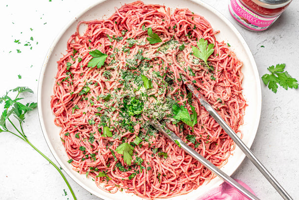 Keto vegan spaghetti on a large white platter with silver tongs next to Primal Kitchen Pink Primavera Sauce and sprigs of parsley