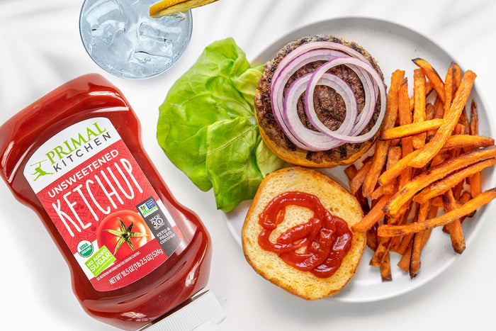 An open face burger on a plate with sweet potato fries next to a bottle of Primal Kitchen Squeeze Ketchup