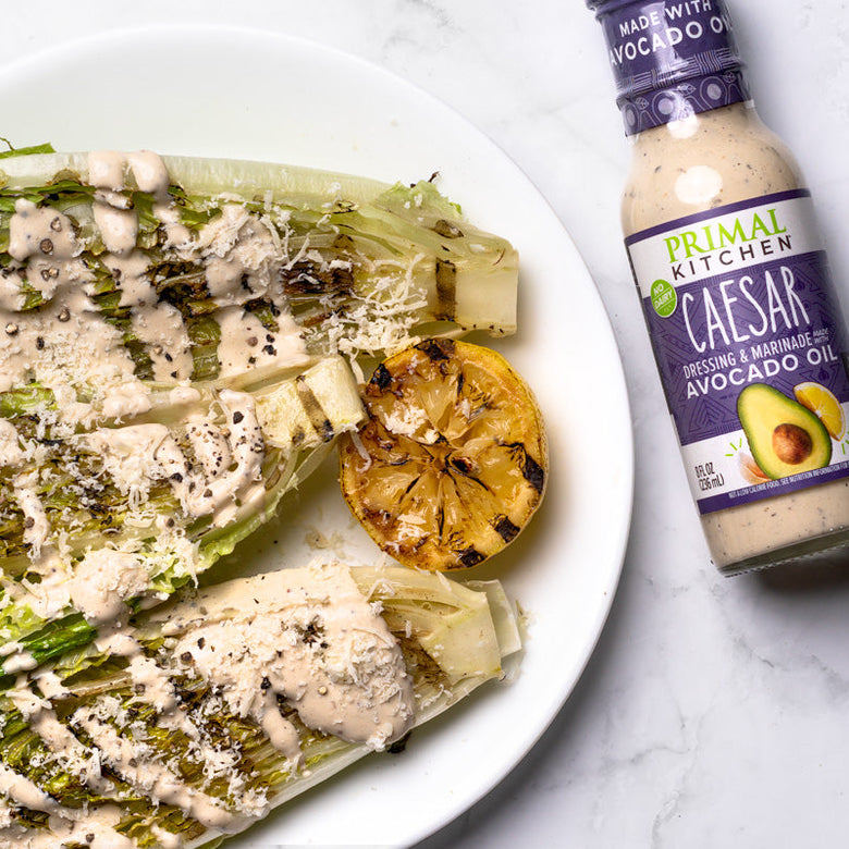 Plated Caesar salad with a bottle of Primal Kitchen Caesar dressing on a marble surface.