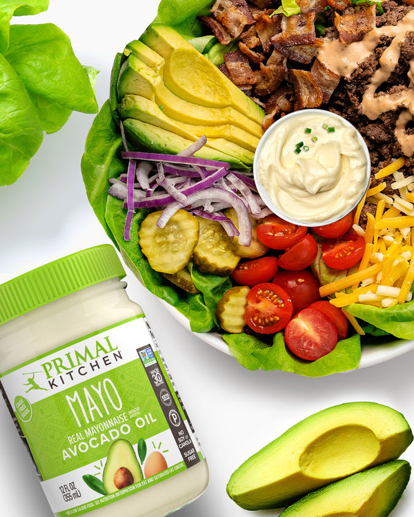 A deconstructed burger bowl next to a jar of Primal Kitchen Mayo and sliced avocados