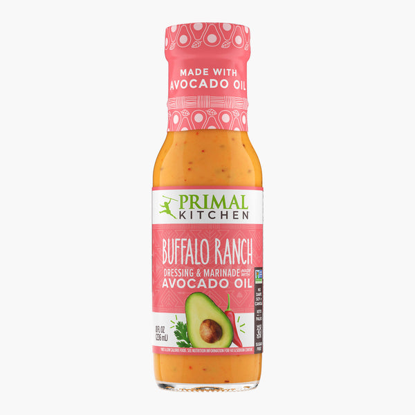 A bottle of no-dairy Primal Kitchen Buffalo Ranch Dressing & Marinade made with avocado oil, with a salmon pink colored label, on a light grey background.