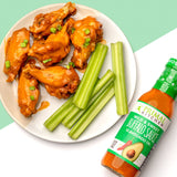 Primal Kitchen Mild and Sweet Buffalo Sauce bottle alongside a plate of Buffalo Chicken Wings and celery on a white and green background