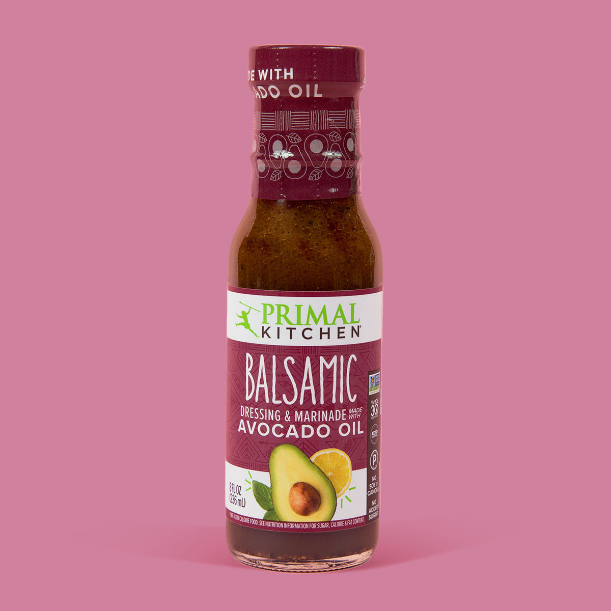 A bottle of Primal Kitchen Balsamic Vinaigrette and Marinade made with Avocado Oil with a dark purple label on a light pink background.
