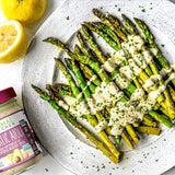Asparagus drizzled with garlic aioli served on a white plate next to lemons and a jar of Primal Kitchen Garlic Aioli.