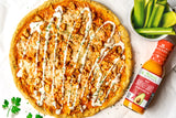 Hot Buffalo Pizza drizzled with ranch dressing, alongside Primal Kitchen Hot Buffalo Sauce and cup of chopped celery