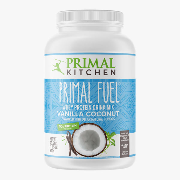 A canister of Primal Kitchen Primal Fuel, a Vanilla Coconut Whey protein drink mix with a blue and white label on a light grey background.