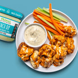 Buffalo caulifllower and veggie sticks on a white plate next to a jar of Primal Kitchen Ranch Dip made with avocado oil. 